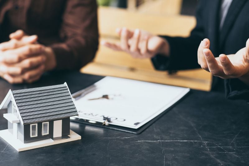 Two people at a desk with a model house and keys during a consultation