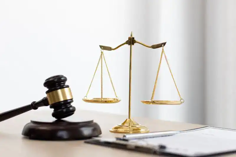 A wooden gavel beside golden scales of justice on a desk with a document