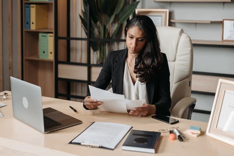 A woman reviewing a document at a desk with a laptop