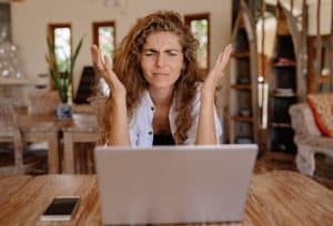 A frustrated woman throwing up her hands at a laptop