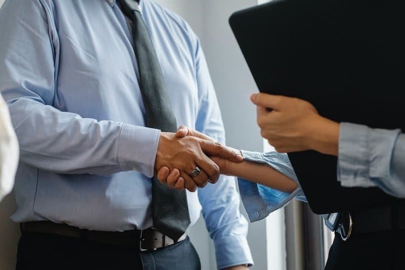 Two people shaking hands while one holds a folder