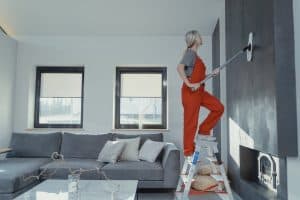 A person in overalls painting an interior wall in a living room