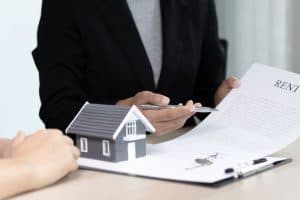 A person at a desk with a model house, keys, and a rental document