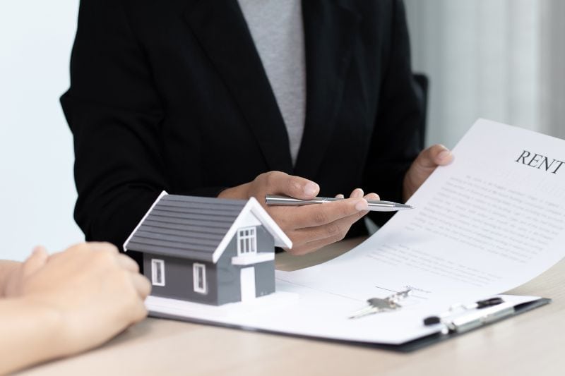 A person at a desk with a model house, keys, and a rental document