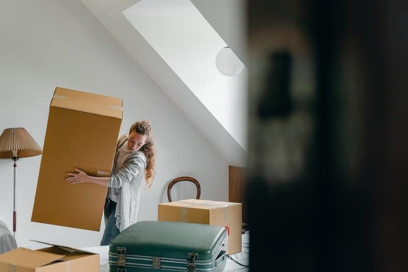 A person carrying a cardboard moving box in an attic room