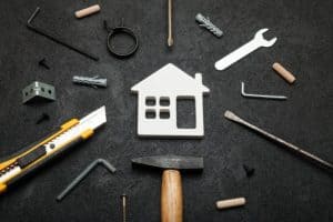 A white house cutout surrounded by repair tools on a dark background