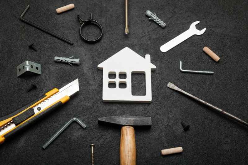 A white house cutout surrounded by repair tools on a dark background