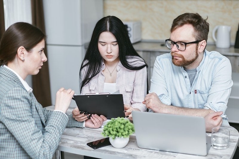 Three people discussing at a table with a tablet and laptop
