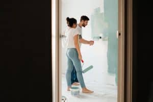 Two people painting an interior room with rollers
