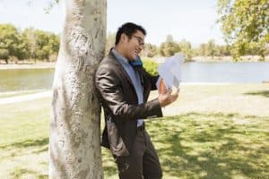 A man in a suit reading a document by a tree in a park