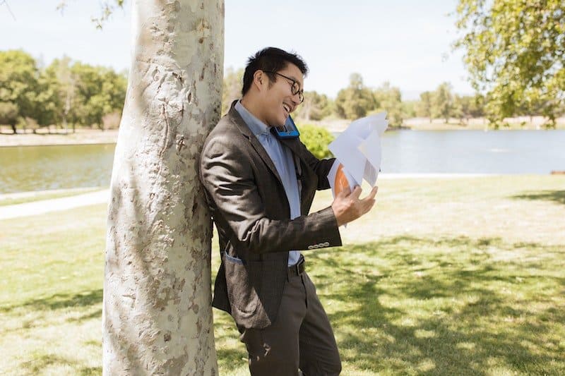 A man in a suit reading a document by a tree in a park