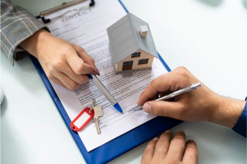Two people signing a contract with a model house and keys on the desk