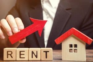 A hand raising a red arrow over a model house with RENT blocks