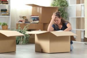 A stressed woman among moving boxes holding her head