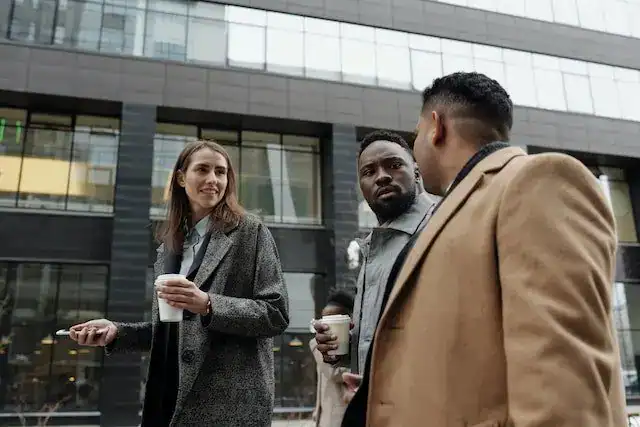 Three professionals in business attire talking outside a building while holding coffee cups